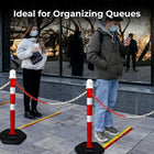 People standing behind red and white striped posts on a sidewalk 