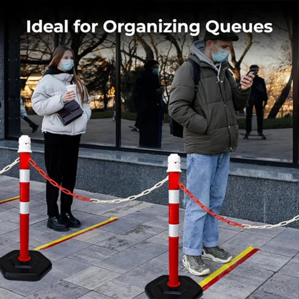 People standing behind red and white striped posts on a sidewalk 