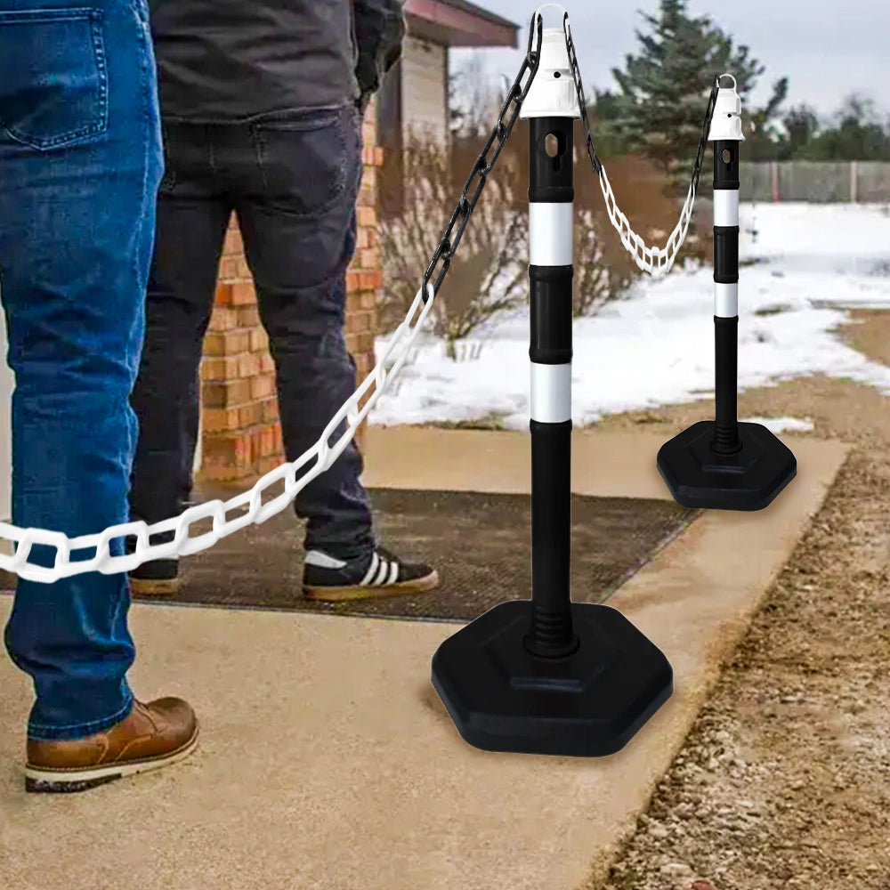 Two people standing on a sidewalk with black and white traffic posts and chain.
