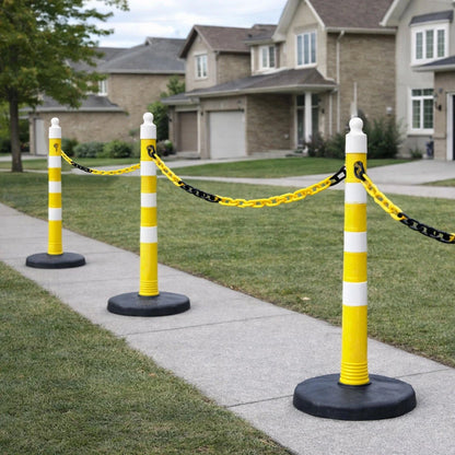 Yellow and white traffic poles with black chains on a sidewalk in front of a house.