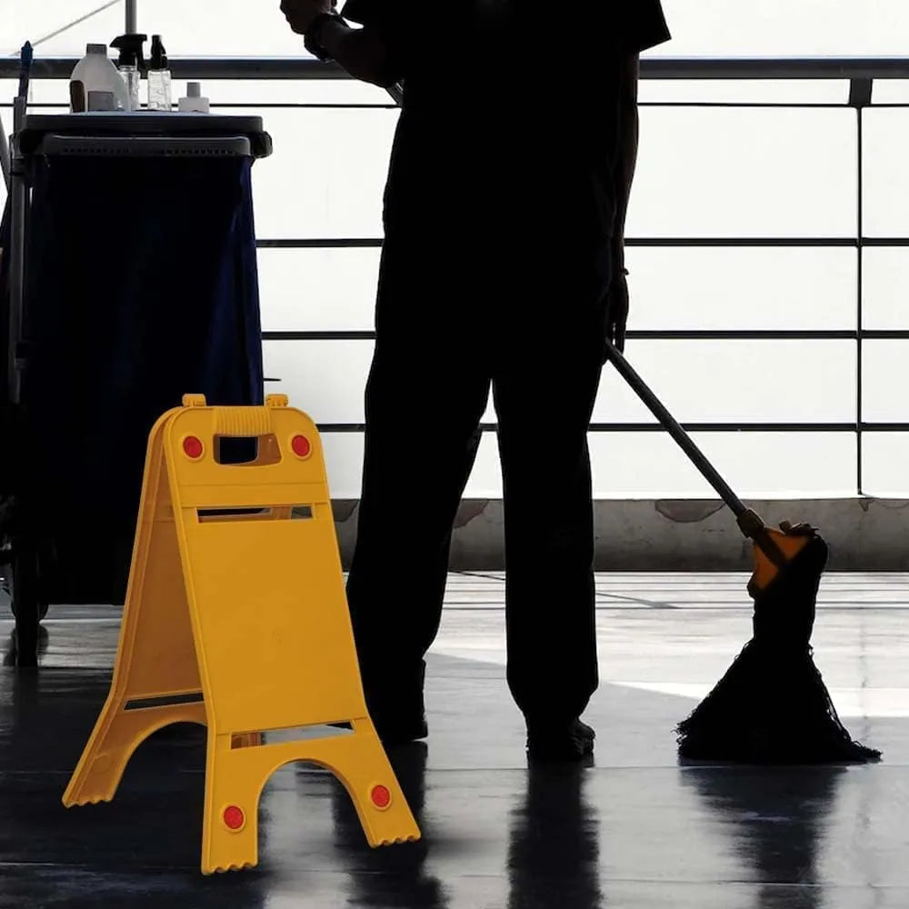 Person cleaning a floor with a mop, next to a yellow safety sign.