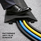 Black shoe stepping onto a patterned anti-slip surface with cables visible.